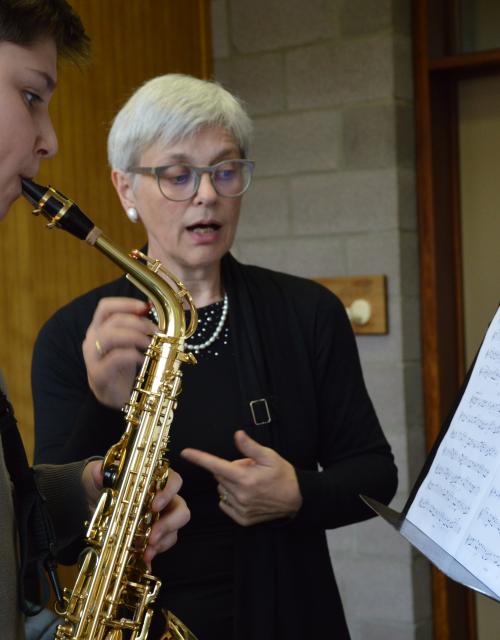 Leerkracht begeleidt leerling bij het spelen van saxofoon